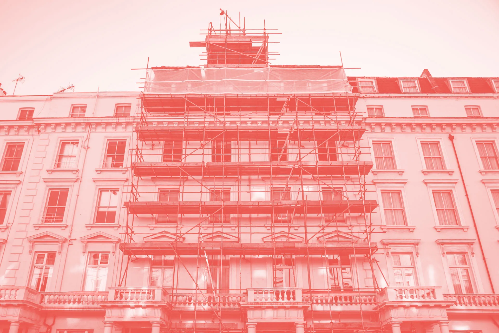 A red photo of a tall building with scaffolding around it.